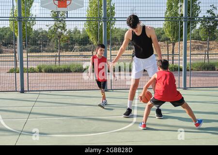 Basketballtrainer spielt Basketball mit zwei Kindern, eines von ihnen hat eine Beinprothese. Trainer trainiert zwei Kinder. Stockfoto