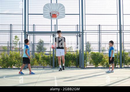 Couch, die mit zwei Schülern Fußball spielt. Einer von ihnen hat eine Beinprothese und sie treten Strafen ein. Stockfoto