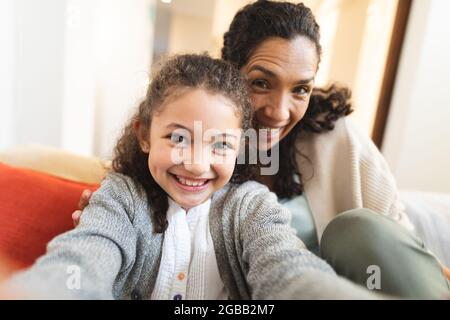 Mutter und Tochter mit gemischter Rasse sitzen auf dem Sofa und machen lustige Gesichter, machen Selfie Stockfoto