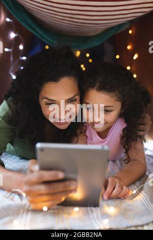 Porträt einer glücklichen, gemischten Mutter und Tochter, die in einem provisorischen Zelt einen Laptop benutzen Stockfoto