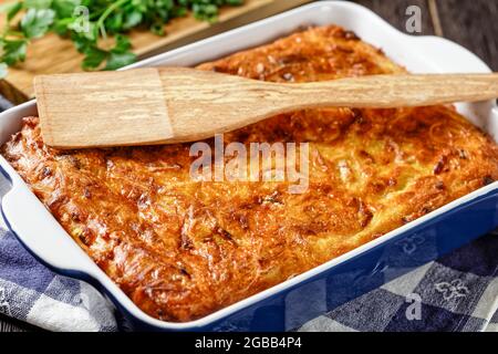 Pikante kartoffelkugel, gebackener Pudding oder Auflauf geriebener Kartoffeln in einer Auflaufform auf einem Holztisch, jüdisches Feiertagsrezept, Nahaufnahme Stockfoto