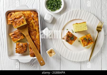 Pikante kartoffelkugel, gebackener Pudding oder Auflauf geriebener Kartoffeln, die in Portionen in einer Auflaufform geschnitten und auf einem weißen Teller auf einem Holztisch, jewis, serviert werden Stockfoto