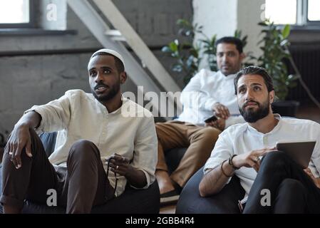 Drei junge, aufmerksame muslimische Geschäftsleute, die dem Redner beim Seminar zuhören Stockfoto