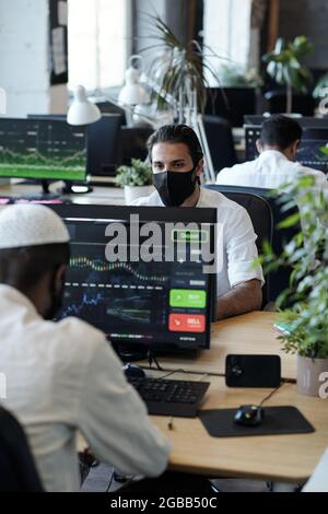 Junger muslimischer Geschäftsmann in Schutzmaske am Computer sitzend Stockfoto