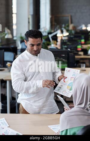 Zeitgenössischer Geschäftsmann mit einem Finanzdokument, das eine Kollegin in einem Hijab während der Diskussion ansieht Stockfoto