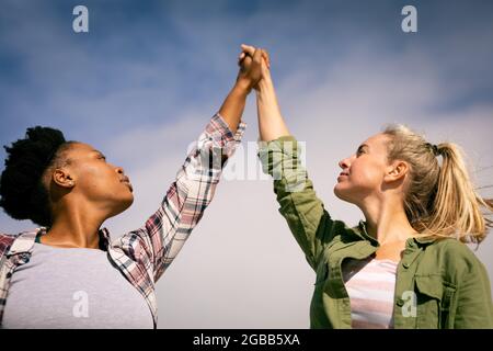 Zwei glückliche, vielfältige Freundinnen halten an sonnigen Tagen die Hände Stockfoto