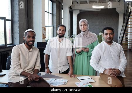 Vier junge zeitgenössische Ökonomen in traditioneller muslimischer Kleidung stehen am Arbeitsplatz Stockfoto