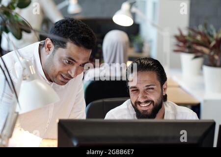 Ein glücklicher junger bärtiger Geschäftsmann und sein Kollege blicken auf den Bildschirm des Computers Stockfoto