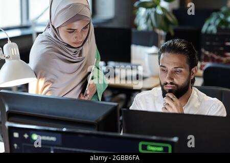 Junge muslimische Geschäftsfrau und Geschäftsfrau, die im Büro vor einem Computermonitor arbeitet Stockfoto
