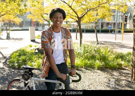Porträt eines afroamerikanischen Mannes in der Stadt, der lächelt und sein Fahrrad hält