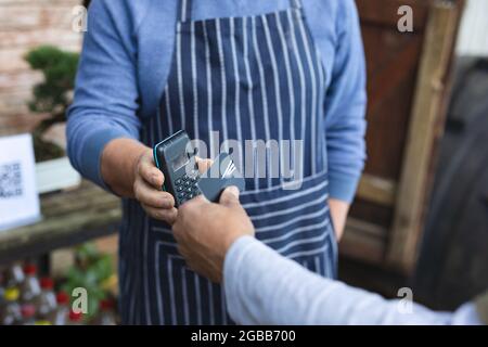 Mittelteil von zwei verschiedenen Männern mit kontaktlosen Zahlungen im Gartencenter Stockfoto