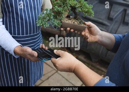 Mittelteil von zwei verschiedenen Männern mit kontaktlosen Zahlungen im Gartencenter Stockfoto