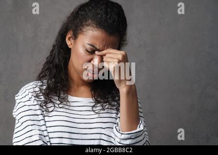 Verärgert gestresste afrikanische Frau, die unter Kopfschmerzen über grauem Wandhintergrund leidet Stockfoto