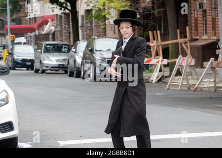 Ein junger orthodoxer jüdischer Mann, der wie ein Teenager aussieht, überquert auf dem Weg zum Morgengebet eine Straße in Williamsburg, Brooklyn. Stockfoto