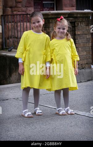 Orthodoxe jüdische Schwestern posieren für ein Foto in passenden gelben Kleidern und weißen Sandalen. An der Bedford Avenue in Williamsburg, Brooklyn, New York City. Stockfoto