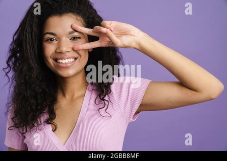 Junge schwarze Frau lacht während gestikuliert Friedenszeichen isoliert über lila Hintergrund Stockfoto
