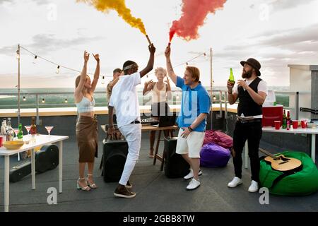 Junge ekstatische Freunde benutzen Feuerwerkskörper mit rotem und gelbem Rauch beim Tanzen Stockfoto