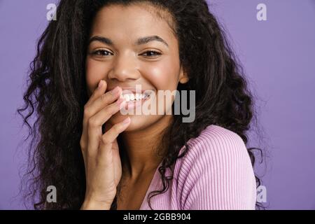 Junge schwarze Frau lacht und bedeckt ihren Mund isoliert über purpurem Hintergrund Stockfoto