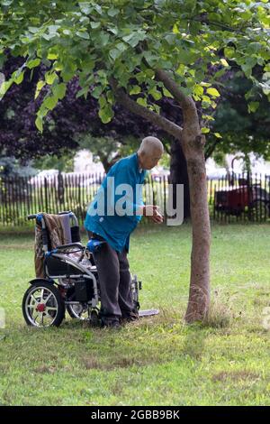 Ein 86-jähriger Mann macht in der Nähe eines Baumes langsam laufende Falun Gong-Übungen. In Queens, New York, ein sehr vielfältiger Ort. Stockfoto