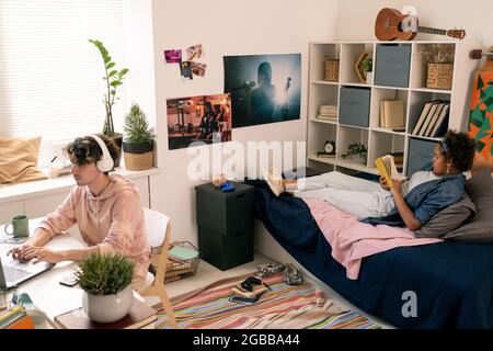 Zwei moderne, erholsame Teenager, die im Schlafzimmer Bücher lesen und sich mit anderen vernetzen Stockfoto
