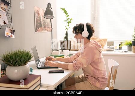 Junger Mann mit Kopfhörern am Schreibtisch und Networking vor dem Laptop Stockfoto