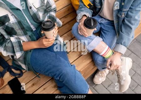 Jugendliche in legerer Kleidung trinken, während sie draußen auf einer Holzbank sitzen Stockfoto