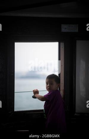 Ein kleiner chinesischer Junge schaut aus dem Fenster eines Bootes in China Stockfoto