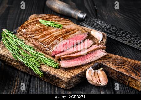 BBQ gegrillte Flanke oder Lasche Rindersteak auf einem hölzernen Schneidebrett. Schwarzer Holzhintergrund. Draufsicht Stockfoto