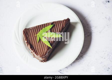 Schokoladenkuchen mit Cannabisblatt - Marihuanablätter Pflanze auf weißem Teller auf dem Holztisch, Cannabisfutter Natur Kräuter Konzept Stockfoto