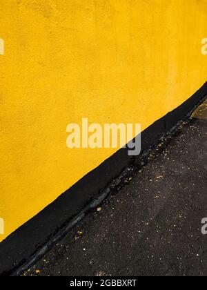 Gelbe Wand des Hauses und schwarzer Asphalt. Bildschirmschoner auf Ihrem Desktop. Hochwertige Fotos Stockfoto