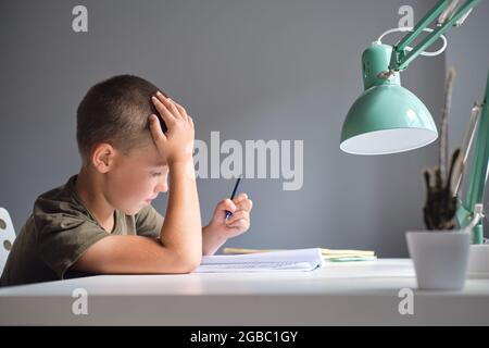 Der Junge sitzt am Tisch und macht zu Hause Schularbeiten. Homeschooling Konzept. Stockfoto