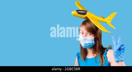 Die Pose des fröhlichen Mädchens in medizinischen Handschuhen und Maske mit dem Spielzeug Luftflugzeug auf ihrem Kopf gelbe Farbe. Stockfoto