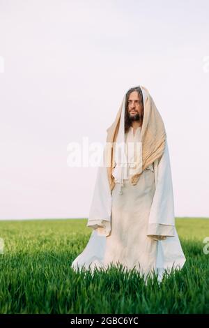 Jesus Christus steht auf einer Wiese, bekleidet mit seiner traditionellen weißen Robe vor dem Hintergrund des Himmels. Stockfoto