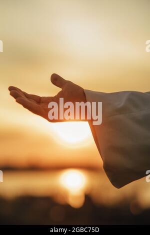 Jesus Christus streut seine Hand vor dem Hintergrund des Sonnenuntergangs zur Hilfe. Nahaufnahme. Stockfoto