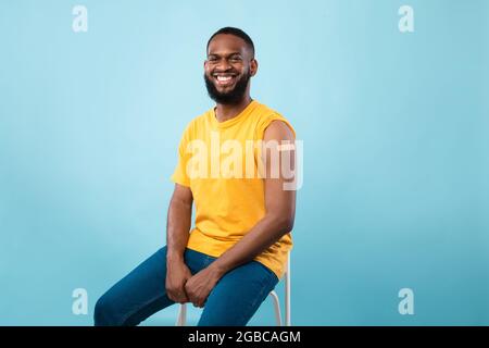 Lächelnder schwarzer Patient mit geimpftem Arm und Bandhilfe nach Immunisierung gegen Covid-19 Stockfoto