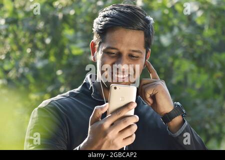 Südindischer Mann mit Smartphone und lächelnd im Park Stockfoto