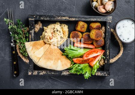 Traditionelle hausgemachte Hummus-Kichererbsen, Falafel, Pita-Brot und frisches Gemüse. Schwarzer Hintergrund. Draufsicht Stockfoto