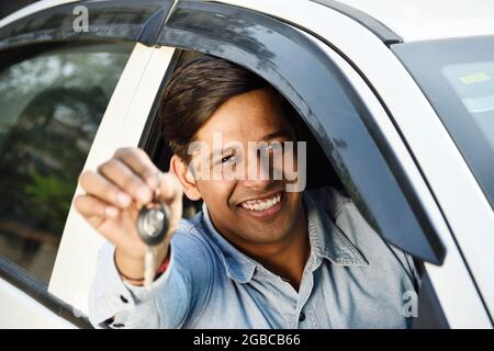 Glücklicher indischer Mann, der den Schlüssel aus dem Auto zeigt Stockfoto