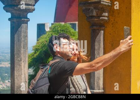 Ein Paar macht Selfies von der wunderschönen Aussicht vom Pena Palace Aussichtspunkt, gelbe und rote Farben des Palastes sind im Hintergrund Stockfoto