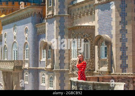 Frau in rotem Kleid posiert vor Blauwall in einem modernistischen Stil Teil des Pena Palace entworfen Stockfoto