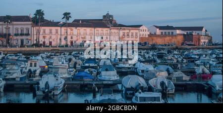 Faro Hafen bei Sonnenuntergang, rosa beleuchtete Gebäude und verlassende Boote im Hafen - Portugal, Panorama Stockfoto