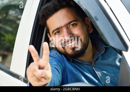 Indischer Fahrer zeigt Siegeszeichen aus dem Auto, Autokredit-Konzept Stockfoto