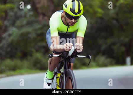 Junger Triathlet, der auf offener Straße ein Fahrrad fährt. Der Profisportler ist am hellen Sommertag im Triathlon engagiert Stockfoto