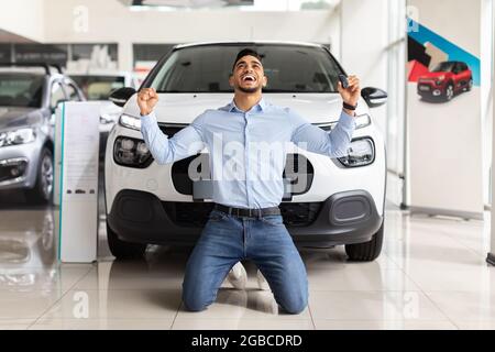 Emotionaler arabischer Kunde, der neben dem Auto kniet Stockfoto