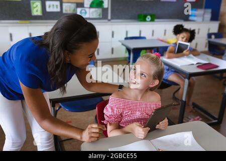 afroamerikanische Lehrerin, die kaukasisches Mädchen unterrichtet, um digitale Tablette an der Grundschule zu verwenden Stockfoto