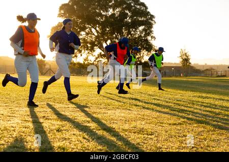 Verschiedene Gruppen von Baseballspielerinnen, die sich bei Sonnenaufgang auf dem Spielfeld aufwärmen und laufen Stockfoto