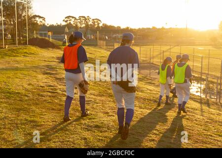 Verschiedene Baseballspielerinnen, die bei Sonnenaufgang zum Training zum Feld gehen Stockfoto