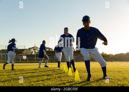 Verschiedene Baseballspielerinnen, die sich bei Sonnenaufgang auf dem Spielfeld aufwärmen und Slalom um Kegel laufen Stockfoto