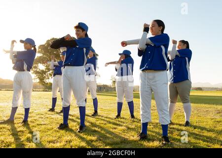 Verschiedene Gruppen von Baseballspielerinnen wärmen sich auf dem Sonnenfeld auf und strecken ihre Arme Stockfoto