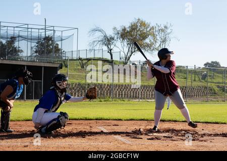 Verschiedene Baseballspielerinnen in Aktion auf sonnigem Baseballfeld während des Spiels Stockfoto